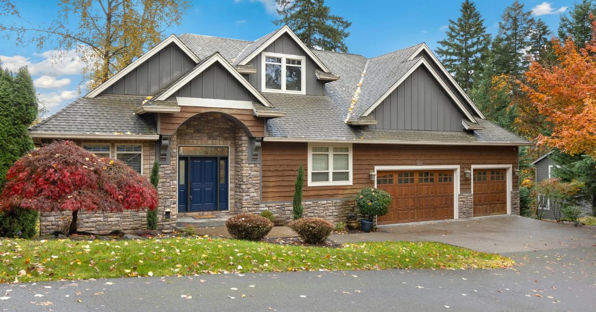 Craftsman-style home with a gray shingle roof, stone entry and wood garage doors