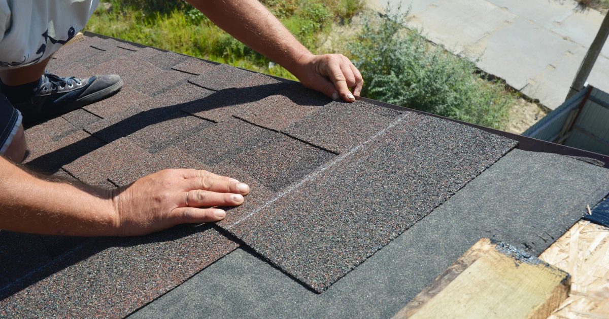 Roofer laying architectural asphalt shingles over underlayment